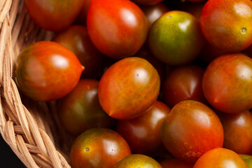 Ripe sweet kumato cherry tomatoes with dark green and red peel in rattan bowl