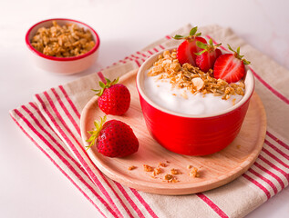 Raw, non-dairy plain yogurt in a red bowl topped with strawberries and granola; plant-based diet; copy space