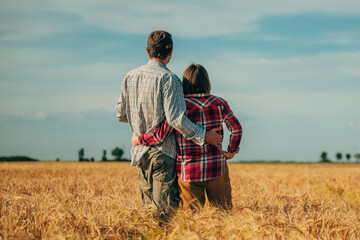 Rear view of male and female farm workers posing in ripe wheat plantation field ready for harvest
