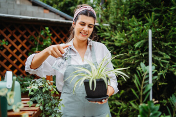 Young woman taking care of plants with water can and mister in garden