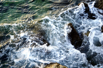 Turquoise sea water splashing stones in the sea and making sea foam