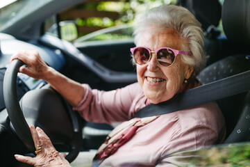 Cool senior woman in sunglasses driving car alone, enjoying car ride. Safe driving for elderly...