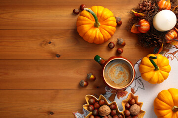 Cozy Autumn background with orange pumpkins, coffee cup, nuts, acorns, candle on wooden table. Flat lay, top view. Autumn, fall, Thanksgiving concept.