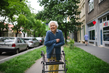 Beautiful elderly woman walking on city street with rollator, going shopping to the store. Feeling cold.