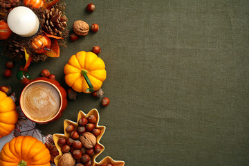 Autumn flat lay composition with pumpkins, coffee cup, decorative candle with pine cones, leaf-shaped plate with nuts, acorns on green cloth table, top view.