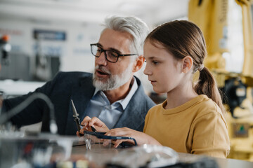 Father and girl during take your daughter to work day, encouraging girl in career in robotics. Teacher showing young schoolgirl how to assemble small robot.