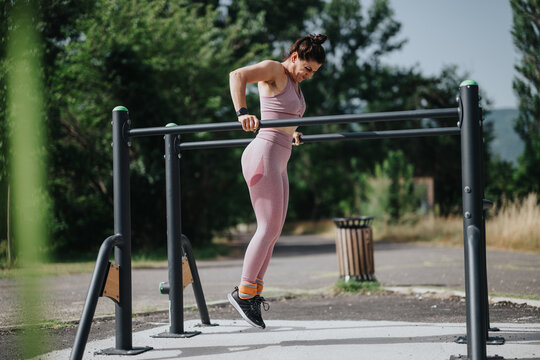 Athletic woman performing calisthenics on parallel bars in a sunny park. Fitness and outdoor exercise concept with focus on strength training.