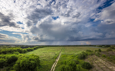 A stunning display of clouds looms over lush, green fields as a gentle rain begins to fall, capturing the beauty of nature at dusk.