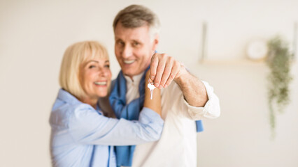 Senior couple moving into new home, man showing keys. Woman embracing husband, panorama