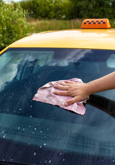 A person is wiping the windshield of a yellow taxi cab