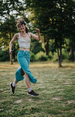 A happy young woman wearing headphones dances energetically in a sunlit park, expressing freedom and joy through modern dance.