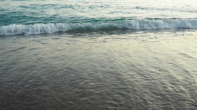 Waves gently lap at shore during stunning sunset over ocean. Golden sunlight reflects off waves as they roll onto shore, creating tranquil atmosphere at sunset by sea. Montenegro summer Canj