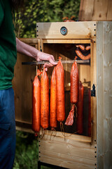 Hand holding homemade sausages and cheese in front of the smokehouse