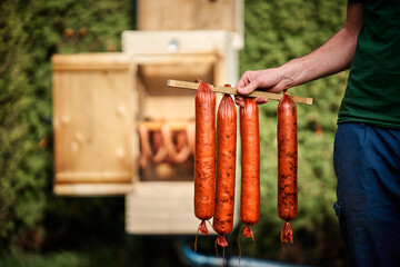 Hand holding homemade sausages in front of the smokehouse