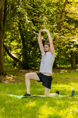 Athletic sporty fit man doing workout yoga breathing exercise on sports mat in park. Raising hands....