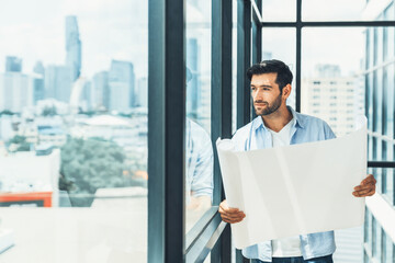 Fototapeta premium Professional architect engineer or male worker in casual outfit looking at skyscraper and city view while holding project plan. Creative design, civil engineering, building construction. Tracery.