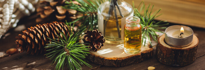 Aromatic home apartment diffuser with the fresh pine fragrance. Spruce, fir tree branches, wooden background. Essential oils, candle as table decor. Cozy atmosphere, Christmas spirit. Banner