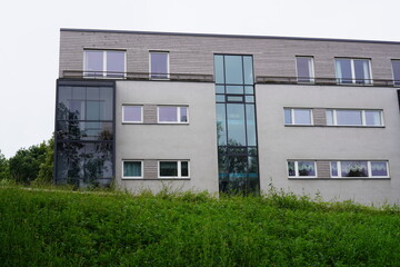 Light grey building with wooden planks, glass blocks. Green grass hill in the front. Summer daytime. Tallinn, Estonia, Europe. July 2024