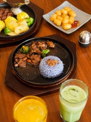 Purplish blue telang flower rice with fried onions on top and thin beef slices on the side on a hotplate