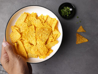 Male hand holds a plate of tortilla chips on a dark gray background.
