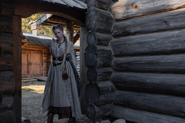 a young girl with a long blond braid in a folk costume, in a village among wooden architecture, Slavic or Nordic style