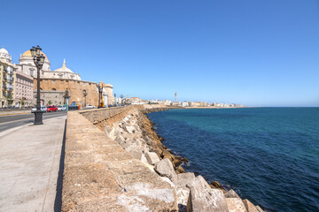 The beautiful promenade of Cadiz, Andalucia, Spain. In the background the cathedral. A beautiful blue sky and blue sea. Vacation, travel, tourism, culture, history.