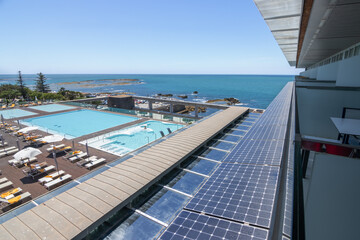 Views of the sea, the pool, people on the sun loungers, solar panels on the façade of the building. Hotel, vacation, tourism, clean energy, travel.