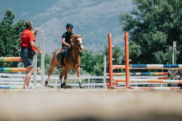 Equestrian rider practicing horse jumping with guidance from instructor at an outdoor riding arena....