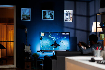 Online gamer enjoying shooter gaming competition at home, participating in multiplayer shooting tournament with friends at night. Young player having fun with video games championship.