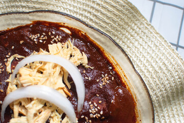 Imagen horizontal, de un plano a detalle de un plato de tortillas con mole rojo con pollo y cebolla  