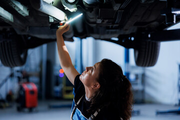 Trained woman working on suspended car in garage, checking tires during routine maintenance....