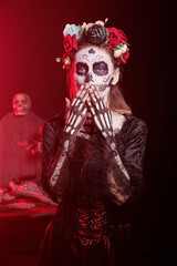 Fototapeta premium Dark lady blowing kisses during Dia de los Muertos, preserving cultural traditions between generations. Woman doing affectionate gesture, wearing la Catrina costume to celebrate Mexican culture
