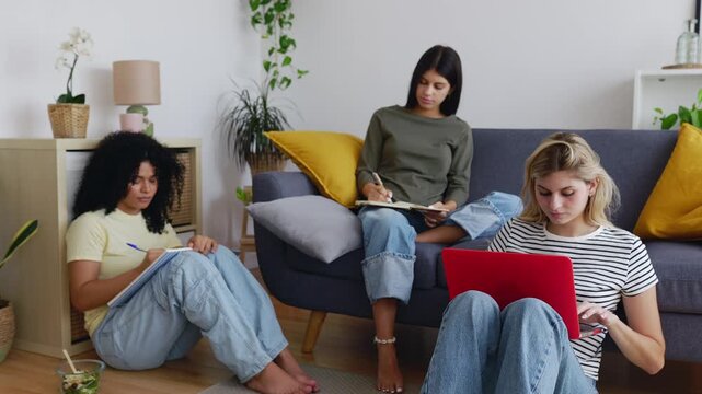 Three young student flatmates girls studying together in the living room. Millennial group of student women working on university assignments at shared apartment. Education life style concept.
