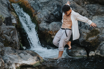 Athletic young man exploring a rocky setting with a waterfall and natural surroundings, showcasing fitness and adventure in nature.