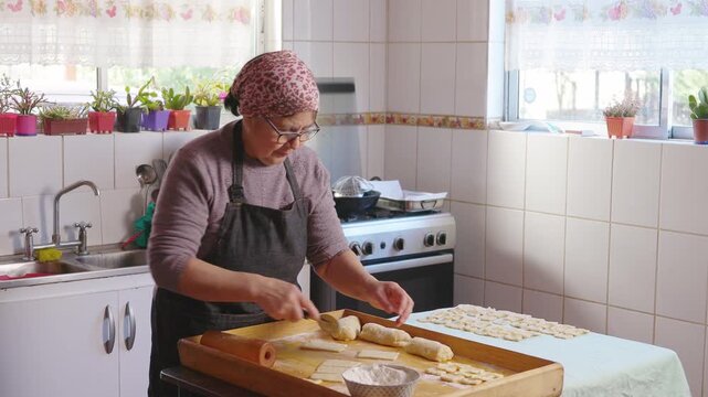 Hispanic senior woman cooking and preparing homemade meal in her modest traditional domestic kitchen 