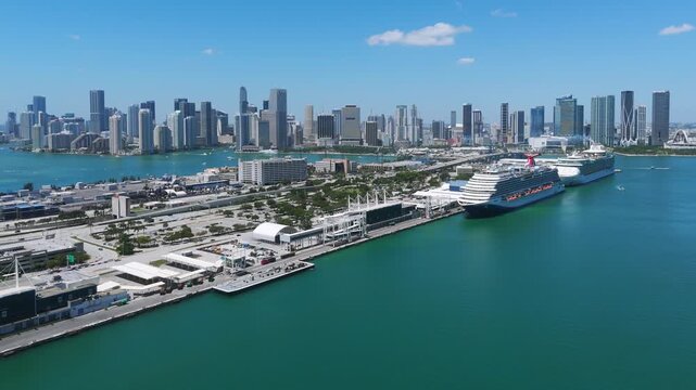 Aerial view of Port Miami with Miami Downtown skyline in background. Port area with multiple large cruise ships docked and various buildings along waterfront