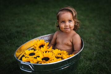 Close up. Cute baby girl mischievous smile, take a bath with sunflowers outdoor.