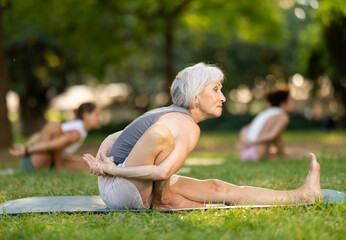 Aged lady in sportwear with group of sporty adult people training stretching workout legs at light...