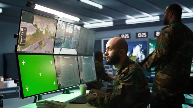 Army soldier looking at chroma key screens in command center housing operational missile defense system designed to intercept ballistic rockets. Specialist using mockup tracking gear, camera B