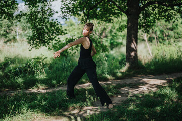 Young woman gracefully performing modern dance in a serene forest setting on a sunny day.