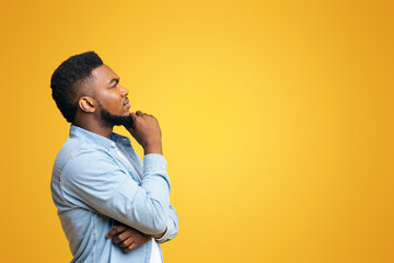 Let me think about it. Profile portrait of thoughtful african american guy on yellow studio background with copy space, panorama © Prostock-studio