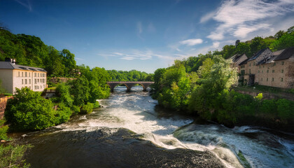 Scenic river flowing through lush greenery with a bridge and buildings