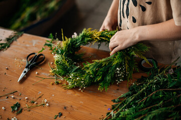 Close-up of a child’s hands crafting a green wreath, intricately weaving natural materials together.