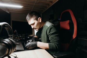 A young man is repairing a laptop in the room in the evening.