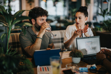 Businesspeople discussing project details over a laptop and tablet during a meeting at a coffee bar.