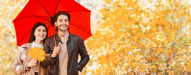 Beautiful young couple with umbrella and bunch of golden marple leaves walking by autumn forest,...