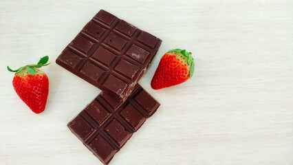 Fresh strawberries and chocolate bars on wooden background with copy space
