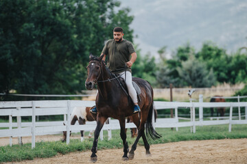 Man enjoying horseback riding at an outdoor equestrian facility surrounded by lush greenery and scenic mountains.