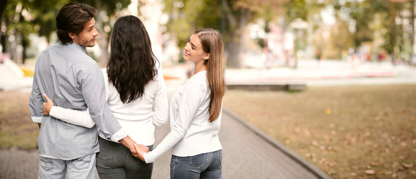 Infidelity. Cheating Boyfriend Holding Hands With Girlfriend's Best Friend Walking Together In Park Outdoors. Back View - Powered by Adobe