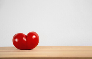Heart shaped red tomato on empty cutting board with space for text or product placement.